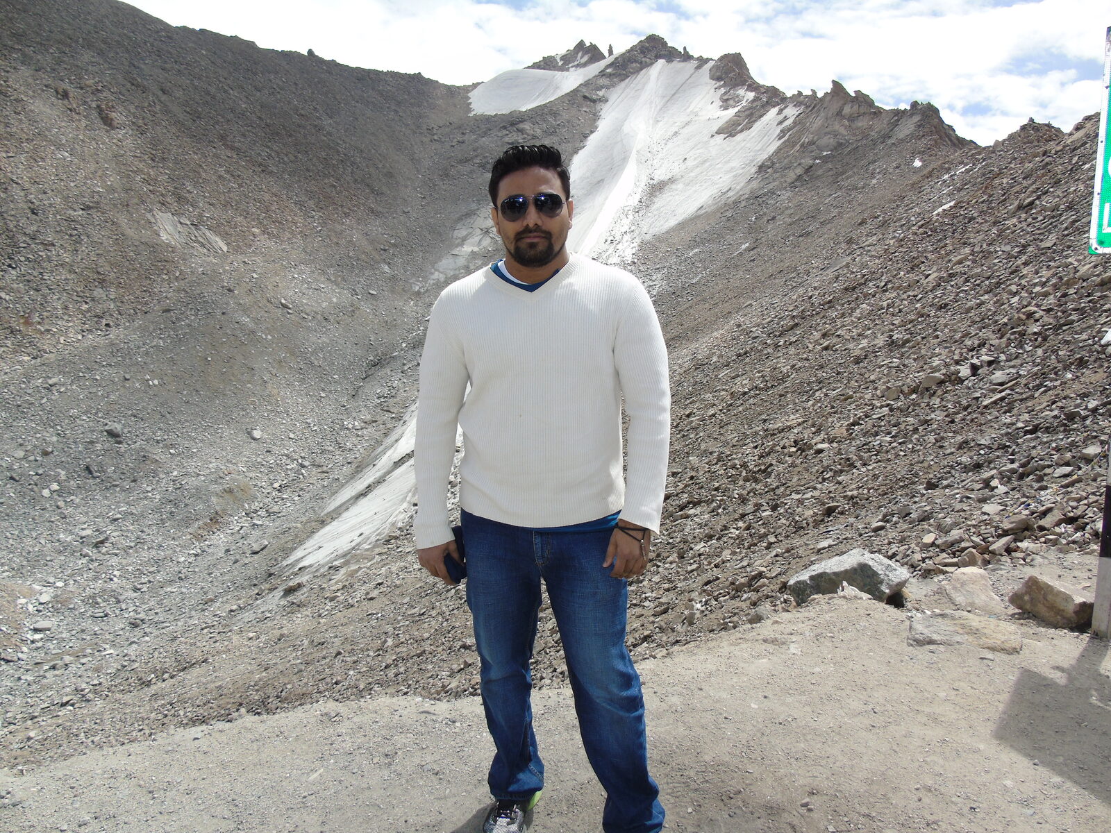 Vinaay Patil standing before a glacier in the Himalayas, wearing a white sweater.